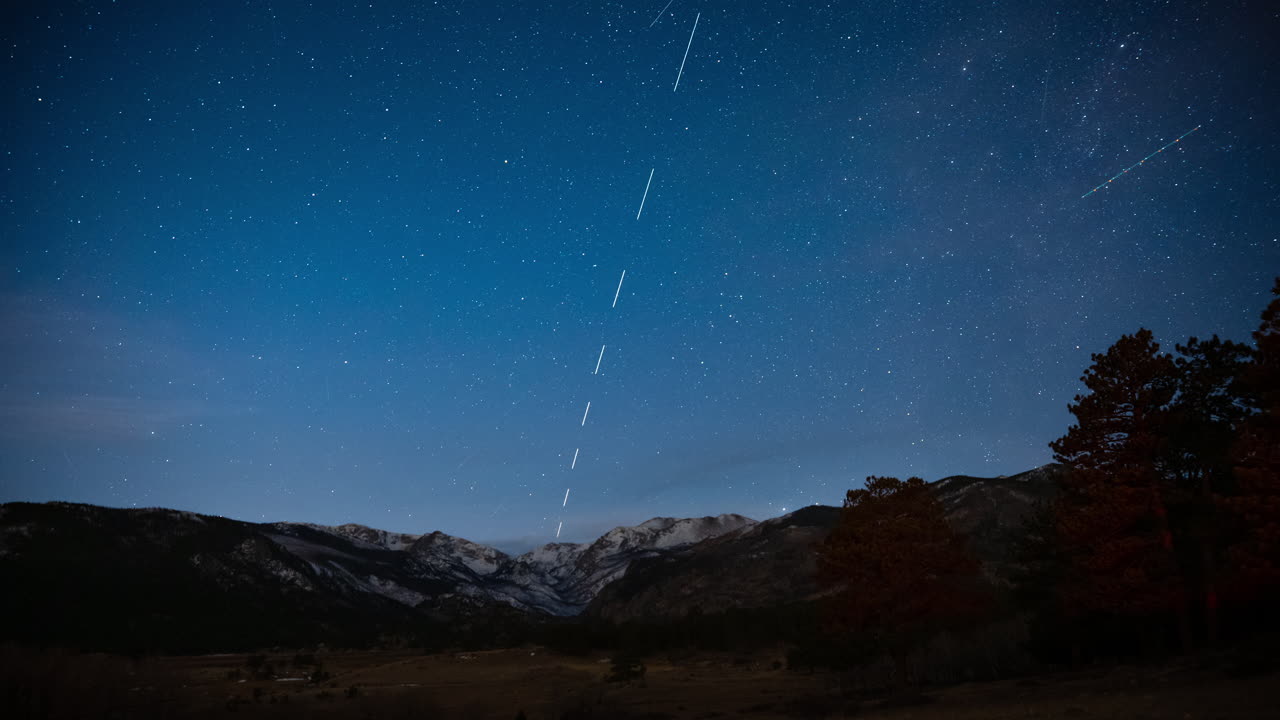 La Vía Láctea sobre el Parque Nacional de las Montañas Rocosas, cielo estrellado con aviones y satélites, time lapse