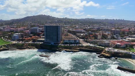 Vista-Aérea-De-Un-Edificio-De-Oficinas-De-Gran-Altura-Con-Olas-Rompiendo-En-Shell-Beach-Y-Piscina-Infantil-La-Jolla-En-California,-Estados-Unidos