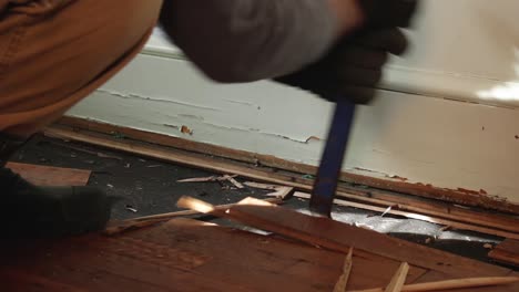 primer plano de un trabajador de cuello azul que quita el suelo de madera dañado por el agua con una barra de palanca azul