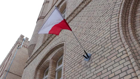 flag of poland attached to brick building waves in breeze