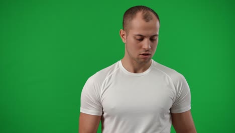 retrato de disparo medio de un joven deportista caucásico girando la pelota de fútbol en el dedo en cámara lenta mirando lejos sonriendo. futbolista positivo y confiado disfrutando del entrenamiento en la pantalla verde de chromakey.