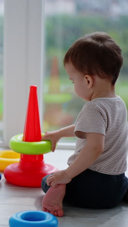 caucasian toddler sits on the floor his back to camera. lovely child playing with toy pyramid. vertical video
