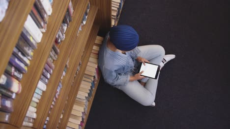 estudiante asiática con un hijab azul sentada en el suelo y usando una tableta
