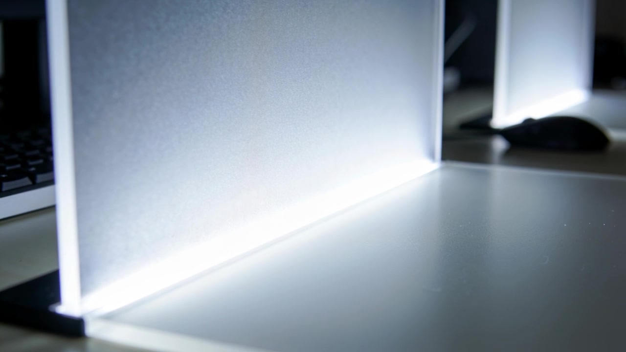 Pannello acrilico traslucido che emette un bagliore LED bianco sulla scrivania, con un secondo pannello, mouse e tastiera.
