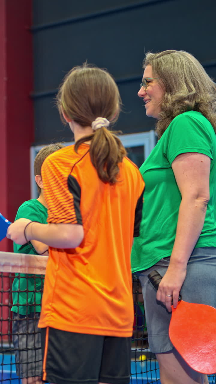 Two adults and two children high-fiving after playing pickleball on a blue, inside court. Vertical