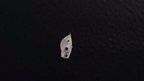 top down aerial view of single small sailboat sailing on dark sea water