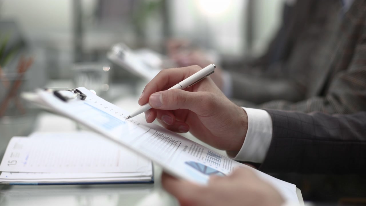 Businessman's Hand Reviewing Financial Report on Clipboard in Office