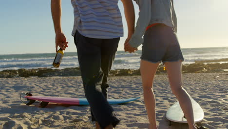 pareja de vista trasera tomándose de la mano con una botella de cerveza corriendo hacia la playa 4k