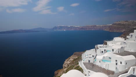 handheld wide shot of a cliff hotel with white buildings and a view of santorini cliffs all the way until the city thira