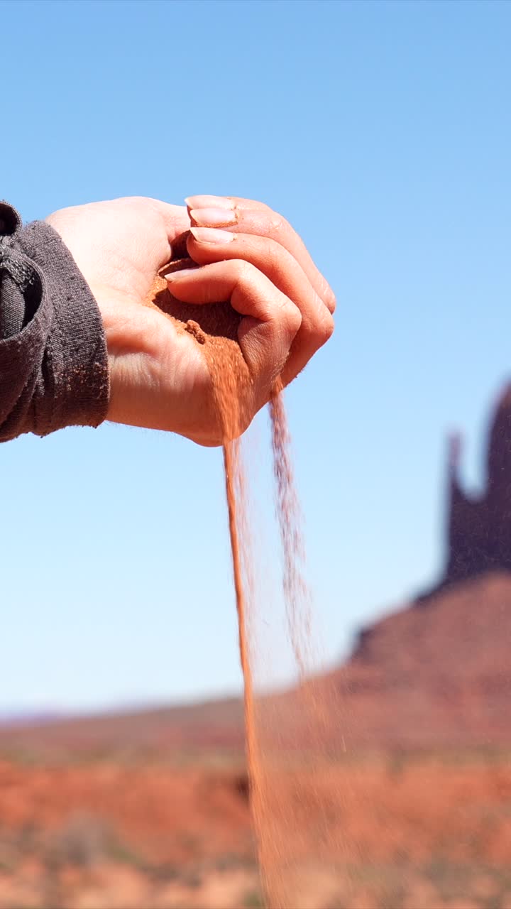 Sabbia rossa del deserto che cade tra le dita di una mano contro un cielo blu