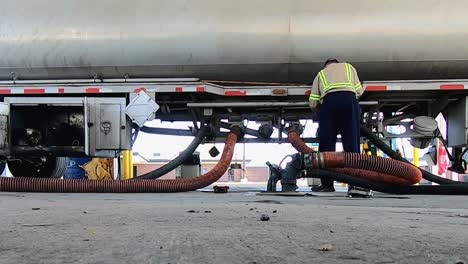 high definition low angle footage of a driver unloading fuel using hoses from a tractor trailer fuel tanker