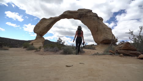 espalda de una mujer joven caminando con una cámara frente a un impresionante arco natural