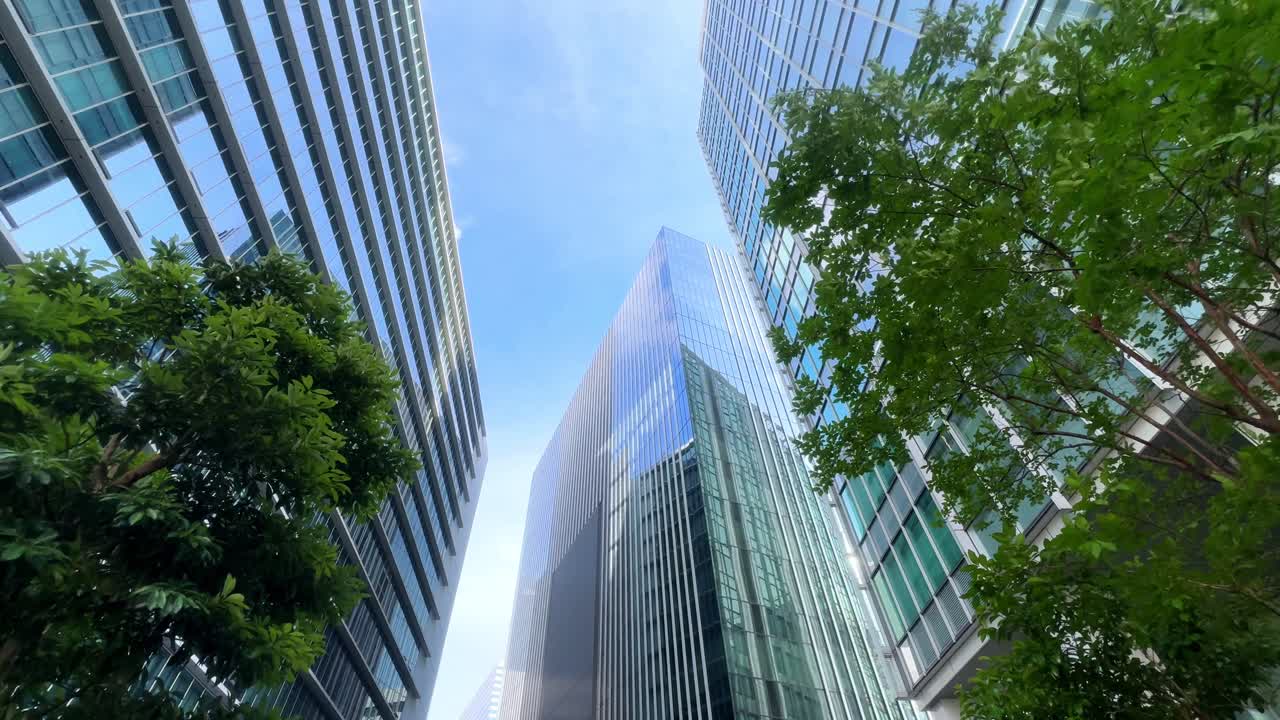 Tall modern skyscrapers surrounded by lush green trees under a clear blue sky