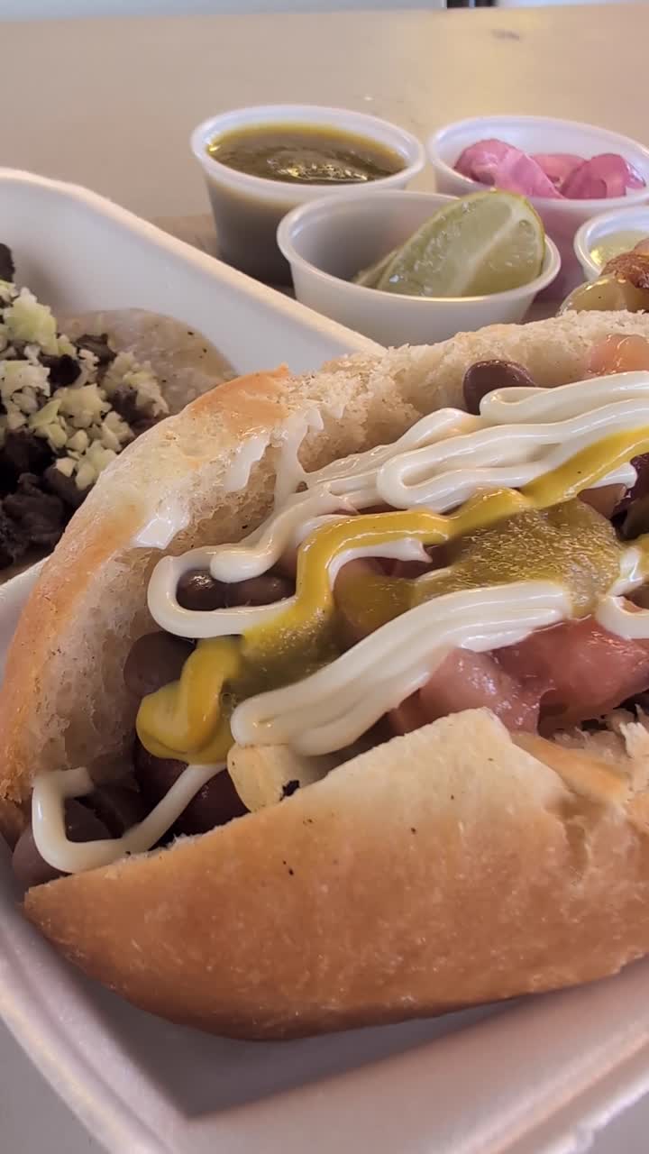 Primo piano verticale di un video di hot dog Sonoran carichi di fagioli, salse e pane morbido. L'inquadratura stretta mette in risalto la texture, i condimenti e la presentazione classica dello street food del sud-ovest