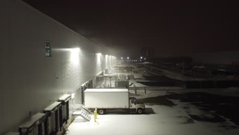 aerial flying beside modern logistics centre at night during cold winters evening over parked lorry and goods left outside