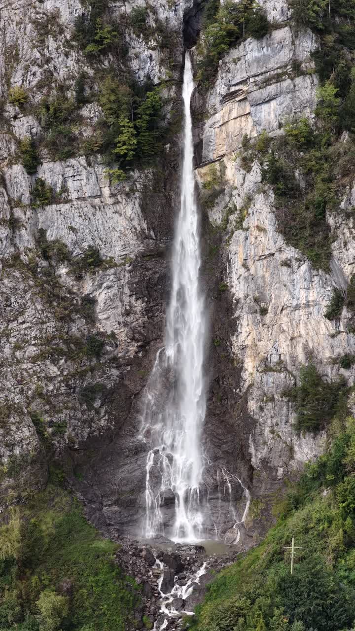 Muslen waterfall in Seerenbach, Schweiz. The water plunges dramatically down a sheer, light gray brown rocky cliff face. The vertical video composition