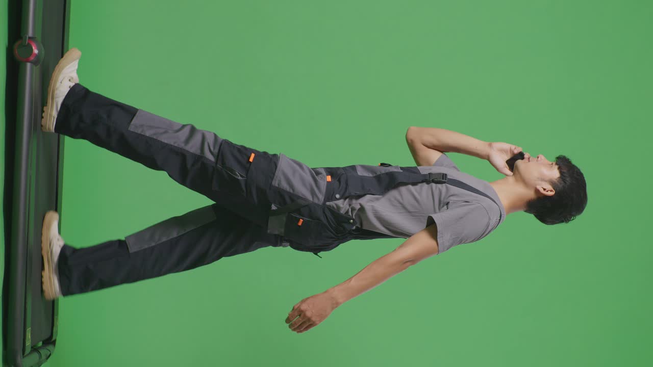 아시아 남성 노동자가 스마트폰으로 이야기하고 녹색 화면 배경 스튜디오에서 는 동안 주위를 둘러보고 있습니다.