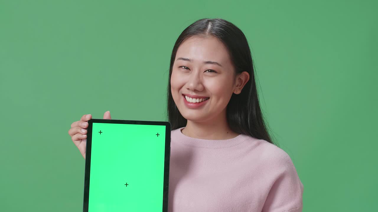 아시아 여성 학생이 녹색 스크린 스튜디오에서 태블릿 녹색 화면 모형을 보여주고 있습니다.