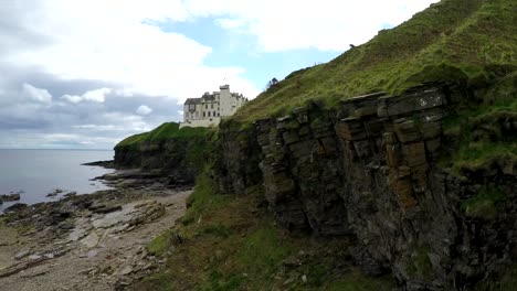 a rising aerial shot of a scottish castle or estate along a cliff