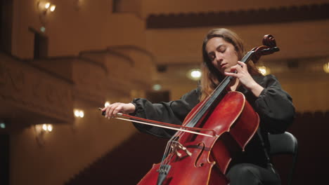 emotional woman is playing violoncello in music hall female violoncellist on scene