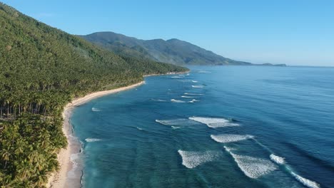 Die-Drohne-Bewegt-Sich-Entlang-Der-Weißen-Sandküste-Und-Dem-Klaren-Blauen-Meer-In-Richtung-Berge