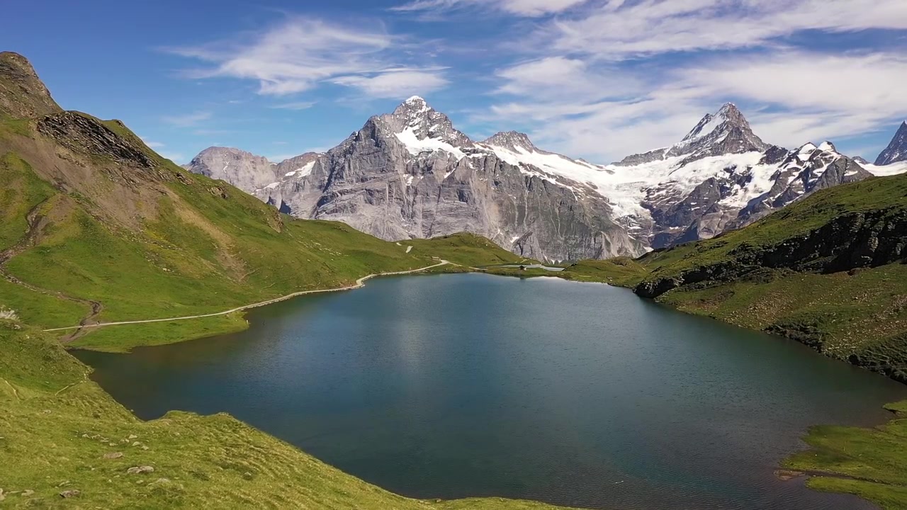 Vista aerea: Lago Bachalpsee nelle Alpi svizzere di Grindelwald, Svizzera. Vista panoramica estiva di un lago alpino di montagna con le cime innevate di Schreckhorn, Wetterhorn e Finsteraarhorn sullo sfondo.