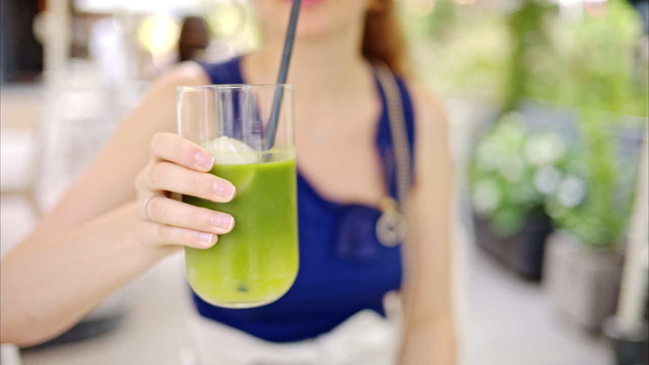 Primo piano al rallentatore di una donna che beve un cocktail matcha con ghiaccio