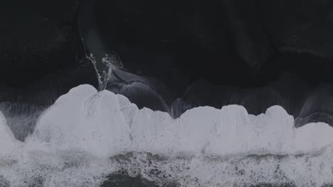 Aerial-top-view-over-ocean-waves-crashing-on-Iceland-Sólheimasandur-black-sand-beach,-on-a-moody-day