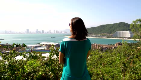 한 여인이 높은 곳에서 바다와 산을 바라보고 있습니다.