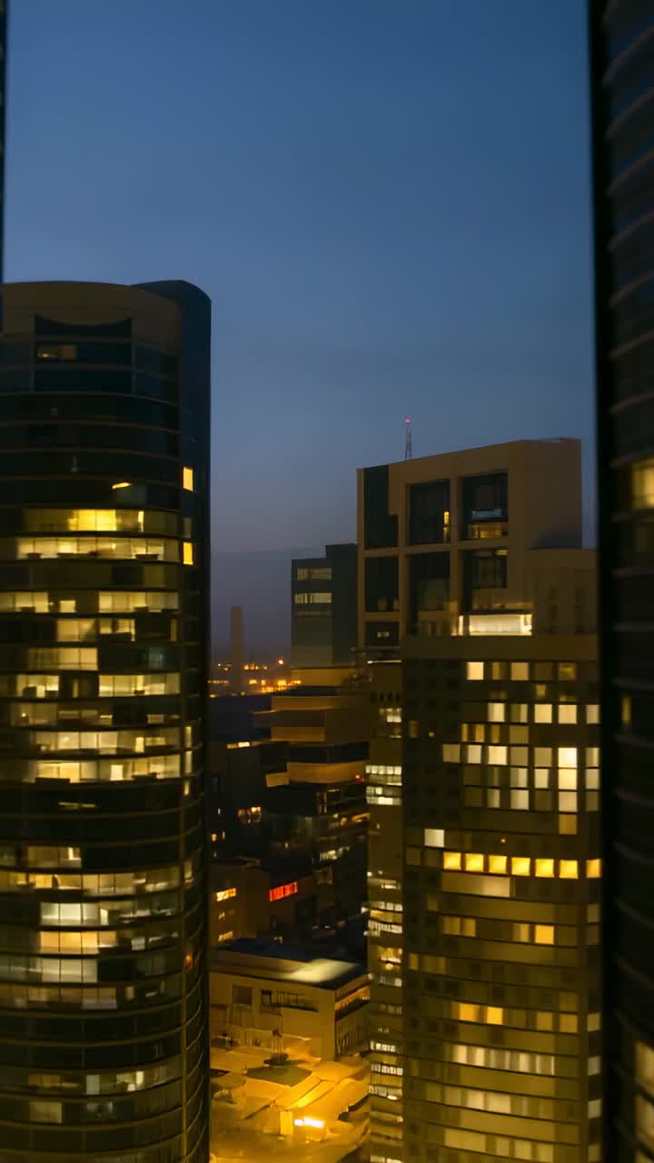 Vertical video: Dimming twilight causing tall towers lighting windows over city skyline at night