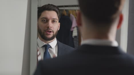 young man in suit at home practising job interview technique reflected in mirror using mobile phone 2