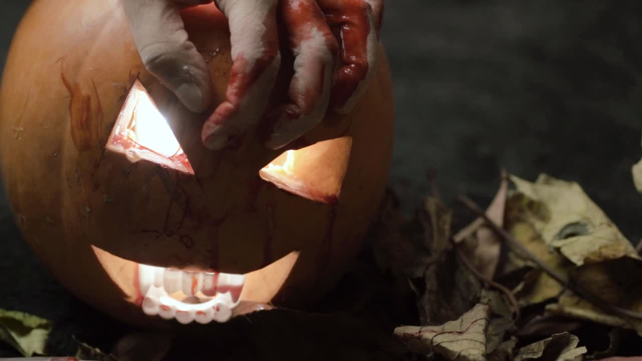 Mani insanguinate che artigliano zucche intagliate di Jack-o'-lantern per Halloween.