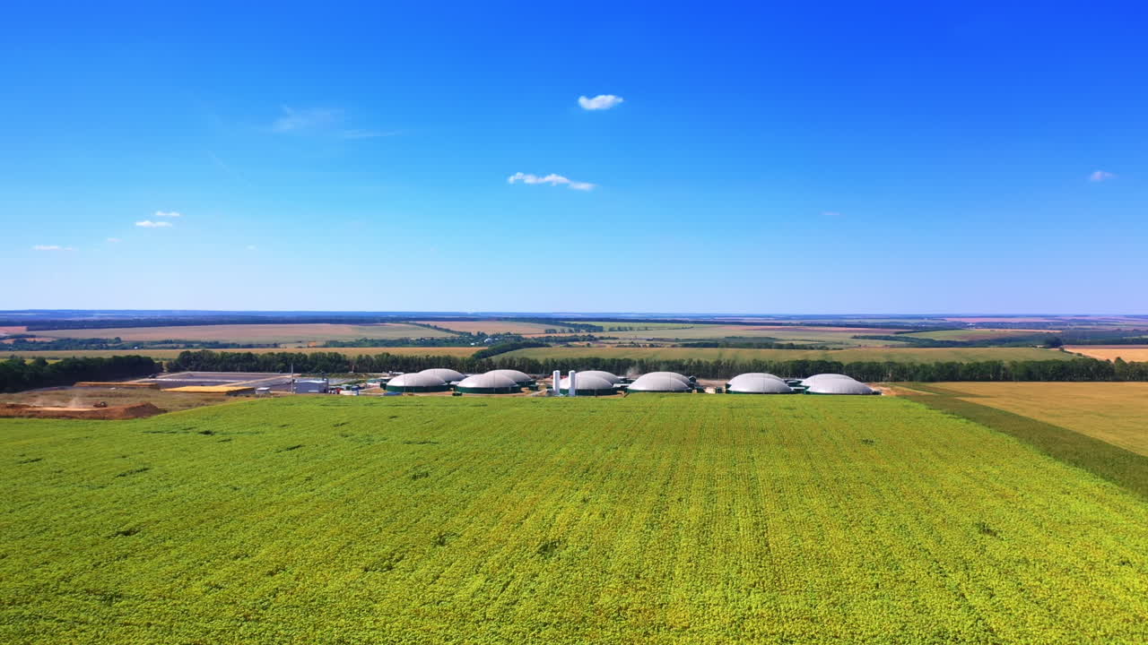Vast farmlands surrounding the modern biogas factory. Drone approaching the cupolas of bio fuel plant. Top view.