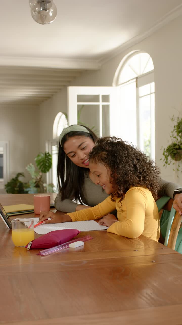 Vídeo vertical: Madre con un lápiz guiando a su hija mientras dibuja formas y letras en la mesa