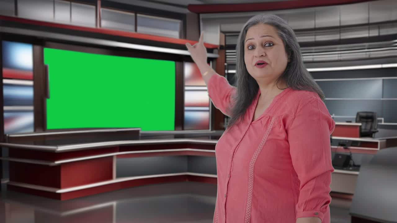 feliz periodista india senior señalando hacia la pantalla verde
