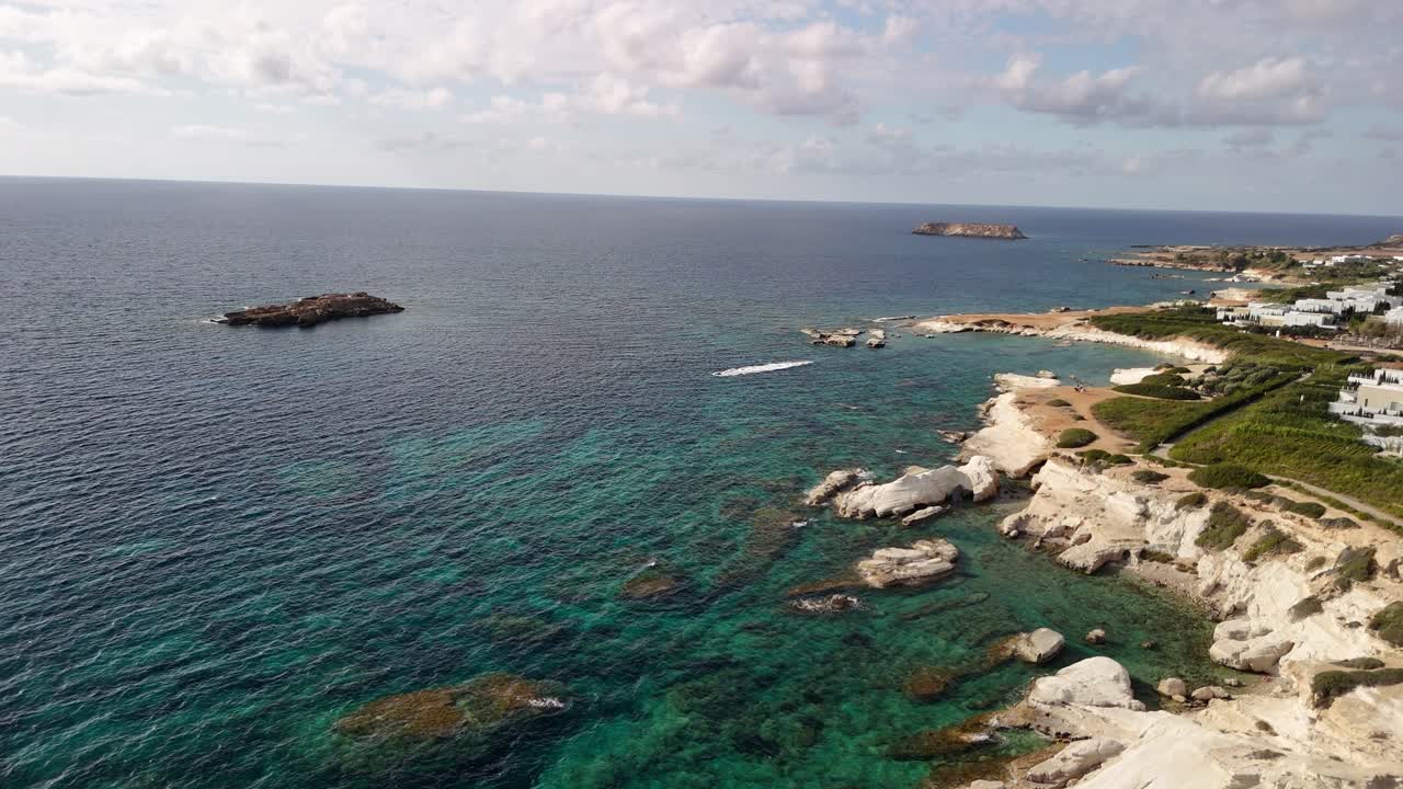Beautiful coastline featuring rocky cliffs and clear turquoise waters. The scene captures small islands in the distance and showcases a peaceful seaside landscape
