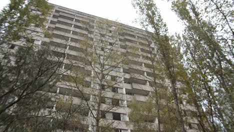 mirando un viejo edificio abandonado a través de árboles en prypiat, chernobyl -inclínate hacia arriba