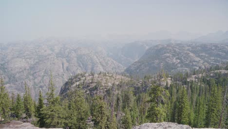 rocky peaks and dense pine forests in a hazy mountain range during a clear summer day