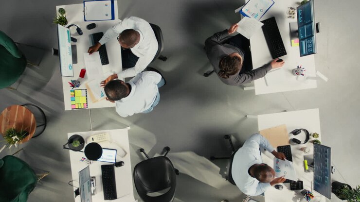 Top-down billede, hvor der zoomes ind på forskellige kollegaer på et kontor, der diskuterer budgettering