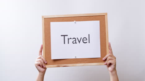 woman's hand shows the paper on board with the word travel in white studio background with copy space