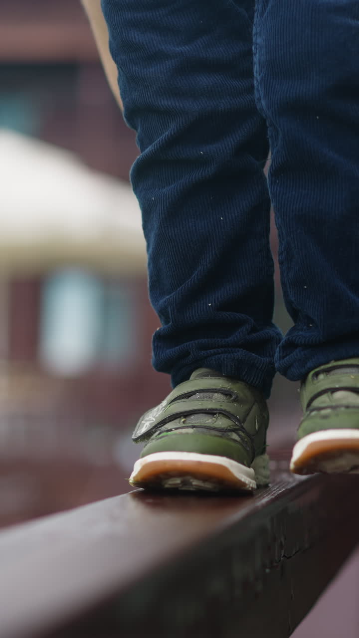 Little boy walks along veranda wooden railing with loving mother help at suburban cottage house on spring day extreme close view slow motion