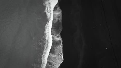 cinematic top down black sand beach aerial, waves crashing on volcanic sand, tilt up revealing mountains, iceland