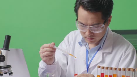 close up of side view of asian man scientist making experiment with test tube and typing on a laptop while working on the table with microscope in the green screen background laboratory