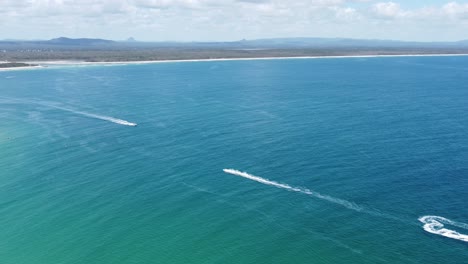 Hoovering-over-the-ocean-jet-skis-below-and-sandy-beach-at-the-background