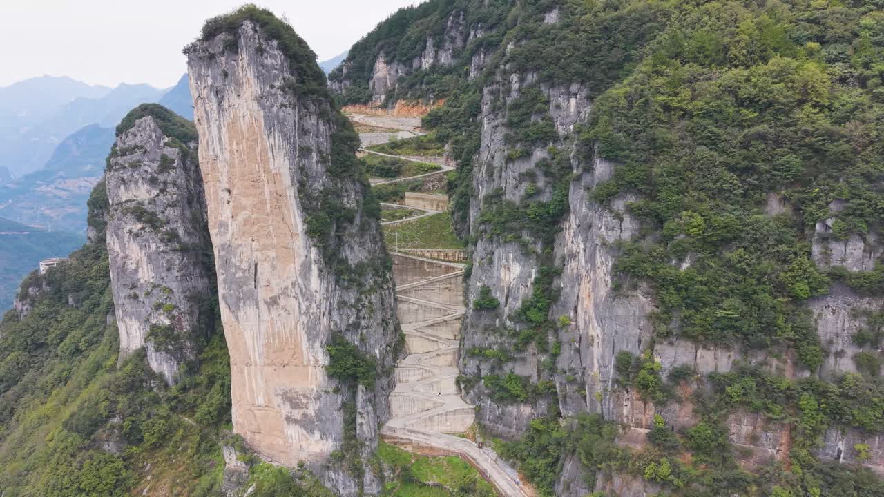 Slow orbiting drone shot of the steep, sheer rock formations and the zigzag road carved into the cliffside at Lingpaishi, Wuxi County, China. Captures remote natural beauty and engineering. UHD
