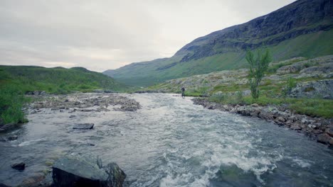 wide static view of lone man fly fishing at stream in northern sweden