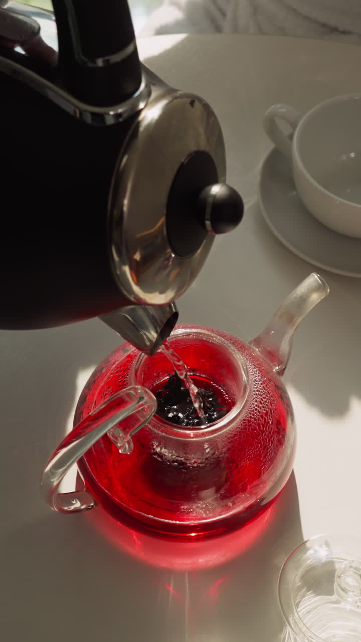 테이블 클로즈업에서 차병에 뜨거운 물을 부어, 그늘진 부에서 아침 식사를 위해 전기 비에서 흐르는 히비스쿠스 차를 우십시오.