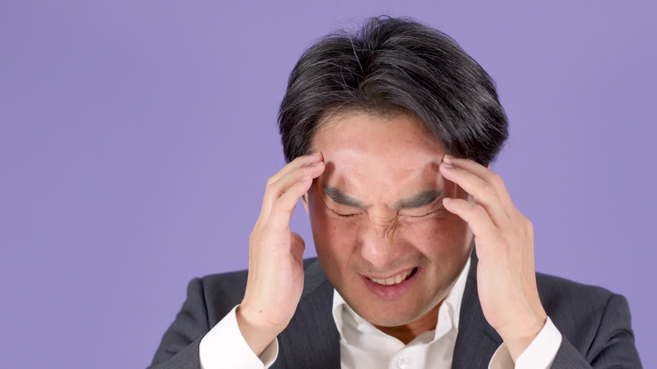 Middle aged businessman in suit massages temples, expressing headache, stress, and mental fatigue