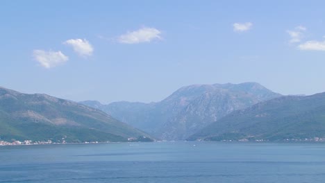 boka kotorska bay, boats sailing over clean adriatic sea water and there is mountains in back with some clouds on blue sky