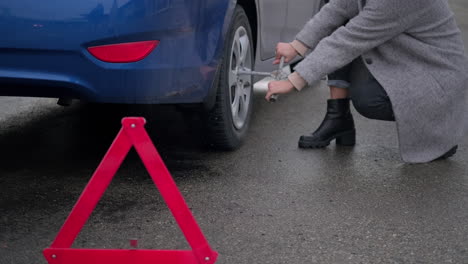 woman changing a flat tire on a rainy day